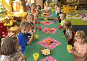 Dzieci siedzą przy stole na którym jest słodki poczęstunek.