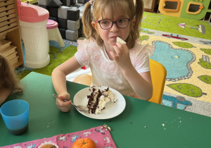 Dziewczynka siedzi przy stole i zajada słodkości.