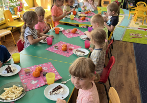 Dzieci siedzą przy stole i zajadają słodkości.