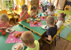 Dzieci siedzą przy stole i zajadają słodkości.