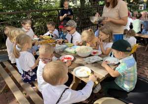 Dzieci siedzą przy stole i zajadają słodki poczęstunek.