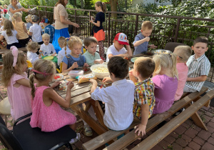 Dzieci siedzą przy stole i zajadają słodki poczęstunek.
