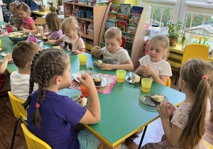 Dzieci siedzą przy stole i jedzą słodkości.