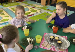 Dzieci siedzą przy stole i jedzą słodkości.