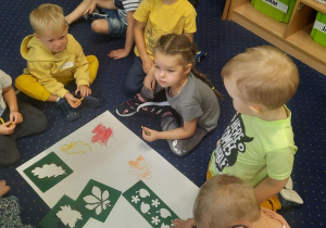 Dzieci siedzą na dywanie i kolorują odrysowane liście.