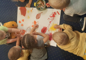 Dzieci siedzą na dywanie i kolorują odrysowane liście.
