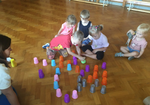 Dzieci siedzą na podłodze i bawią się kolorowymi kubeczkami.
