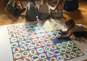Dzieci siedzą na podłodze i układają obrazki zgodnie z kodem.