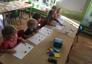 Dzieci siedzą przy stolikach i układają kompozycje z figur geometrycznych.