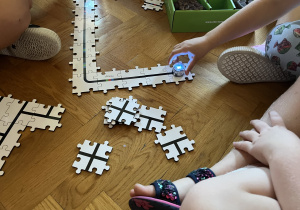 Dzieci siedzą na podłodze i układają drogę z puzzli dla ozobota.