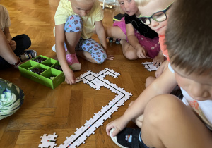 Dzieci siedzą na podłodze i układają drogę z puzzli dla ozobota.