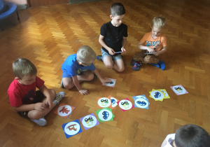 Dzieci siedzą na podłodze i klasyfikują rysunki.