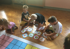 Dzieci siedzą na podłodze i klasyfikują rysunki.