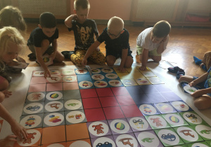 Dzieci siedzą na podłodze i układają rysunki zgodnie z kodem.