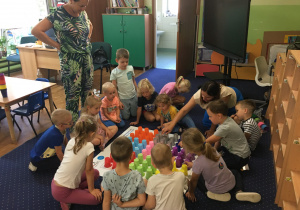 Dzieci siedzą na dywanie i układają kolorowe kubeczki na macie do kodowania.
