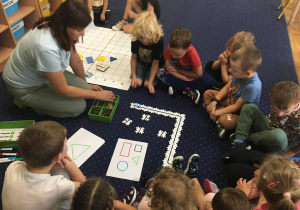 Dzieci siedzą na dywanie i obserwują programowanie ozobota z wykorzystaniem puzzli.