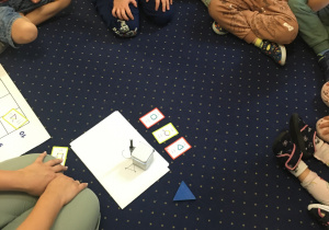 Dzieci siedzą na dywanie i obserwują rysującego genibota.