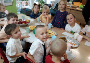 Dzieci siedzą przy stole i degustują owoce.