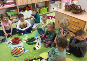 Dzieci siedzą na dywanie, a przed nimi leżą warzywa w obręczach.