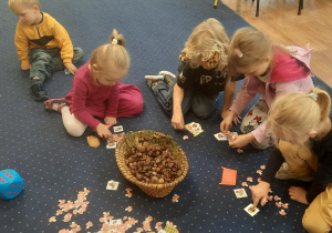 Dzieci siedzą na dywanie i układają dary natury.
