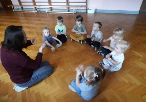 Dzieci siedzą na podłodze i powtarzają sekwencje ruchowe.