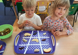 Dzieci siedzą przy stoliku i wykonują owocowe sudoku.