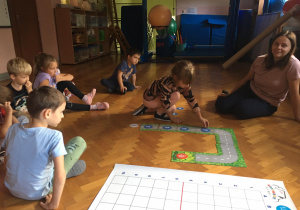 Dzieci siedzą na podłodze i układają drogę z wykorzystaniem znaków.