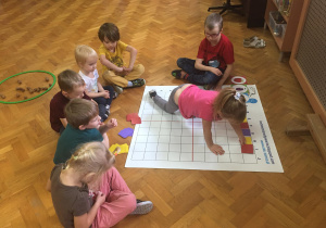 Dzieci siedzą na podłodze i wykonują zadanie na macie do kodowania.