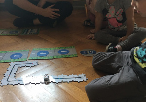 Dzieci siedzą na podłodze i układają drogę dla ozobota z puzzli.