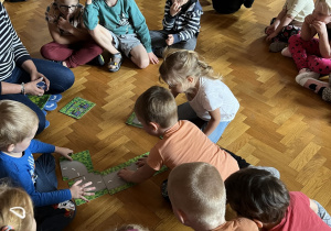 Dzieci siedzą na podłodze i układają drogę z ilustracji.