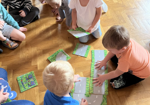 Dzieci siedzą na podłodze i układają drogę z ilustracji.