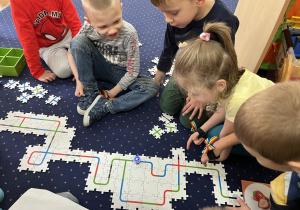 Dzieci siedzą na dywanie i układają drogę z puzzli dla ozobota.