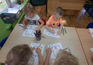 Dzieci siedzą przy stole i kolorują znaki zgodnie z instrukcją.