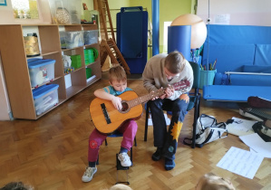 chłopiec trzyma gitarę, starszy chłopiec pokazuje jak prawidłowo chwytać gitarę i na niej grać