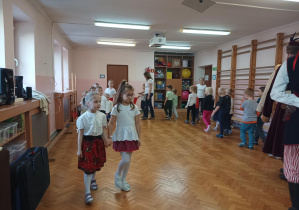 dzieci na sali gimnastycznej tańczą poloneza wraz z osobami ubranymi w stroje ludowe