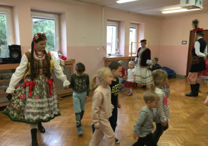 dzieci na sali gimnastycznej tańczą poloneza wraz z osobami ubranymi w stroje ludowe
