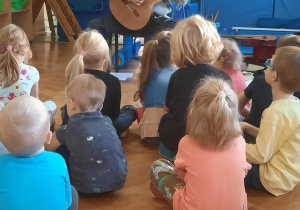 Dzieci siedzą i słuchają muzyki.