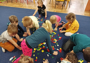 dzieci siedzą na dywanie, układają kompozycje z figur geometrycznych