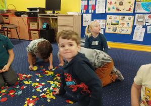 dzieci siedzą na dywanie, układają kompozycje z figur geometrycznych