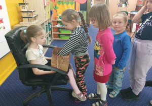 Dziewczynka siedzi na krześle, a pozostałe dzieci podchodzą, składają życzenia i biorą cukierka. a