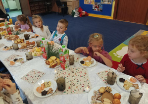 dzieci świętują wigilię przy wspólnym stole pełnym słodyczy i owoców