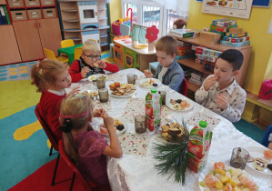 dzieci świętują wigilię przy wspólnym stole pełnym słodyczy i owoców
