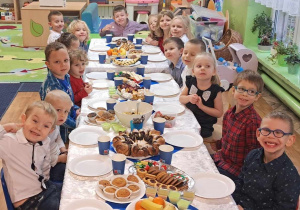 grupa dzieci przy wspólnym stole, na którym widać smakołyki