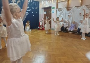 dziewczynki w białych sukienkach tańczą na sali gimnastycznej