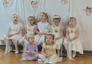 dziewczynki w białych sukienkach siedzą na ławeczce na sali gimnastycznej