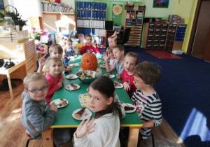 Dzieci siedzą przy stołach i zajadają słodki poczęstunek.