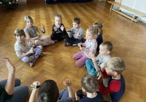 dzieci siedzą na podłodze na sali gimnastycznej podnoszą ręce do góry