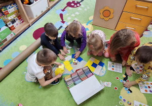 dzieci siedzą w sali na dywanie, układają wzór dla ozobota