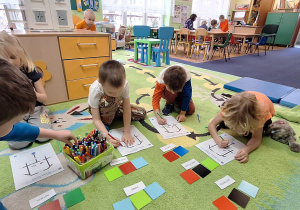 dzieci siedzą w sali na dywanie, układają wzór dla ozobota na białych kartkach