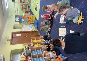 dzieci siedzą na niebieskim dywanie, przed nimi kartki, przybory do higieny